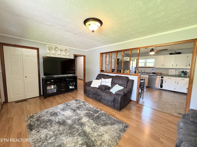 living area featuring a textured ceiling, light wood finished floors, and ornamental molding