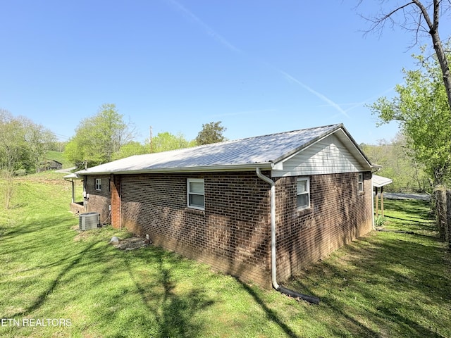 view of side of property with a lawn, central AC unit, and brick siding