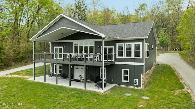 back of house with board and batten siding, a lawn, a patio, and a deck