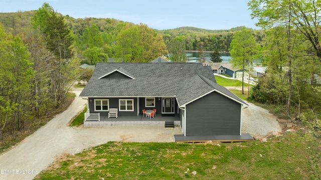view of front facade with roof with shingles, a front lawn, a water view, a wooded view, and covered porch