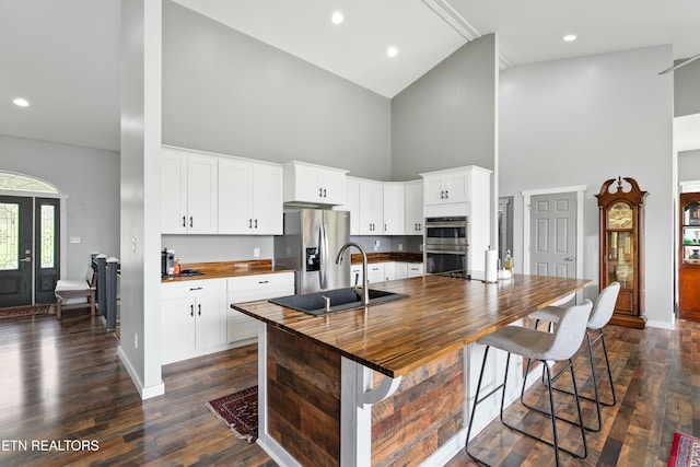 kitchen with a sink, dark wood-style flooring, butcher block counters, high vaulted ceiling, and appliances with stainless steel finishes