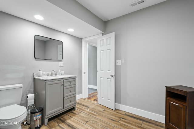 bathroom with wood finished floors, vanity, baseboards, toilet, and visible vents