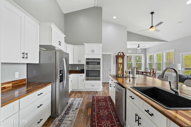 kitchen with high vaulted ceiling, a sink, wood counters, ceiling fan, and stainless steel appliances