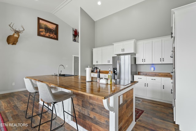 kitchen with a sink, dark wood finished floors, stainless steel refrigerator with ice dispenser, wood counters, and high vaulted ceiling