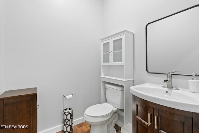 bathroom with toilet, vanity, wood finished floors, and baseboards