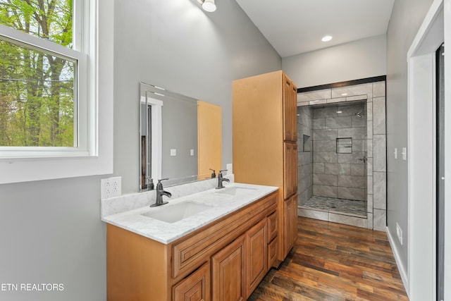 bathroom featuring double vanity, wood finished floors, tiled shower, and a sink