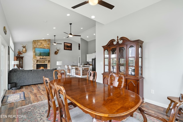 dining room featuring vaulted ceiling, a stone fireplace, a ceiling fan, and wood finished floors