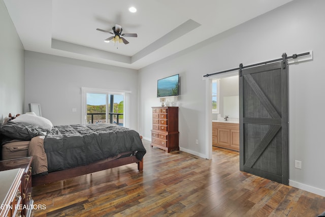 bedroom featuring a barn door, a sink, a tray ceiling, wood-type flooring, and access to exterior