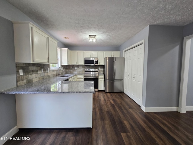 kitchen featuring a peninsula, a sink, baseboards, light stone counters, and appliances with stainless steel finishes