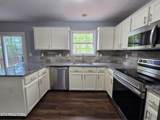 kitchen featuring stainless steel appliances, a peninsula, a sink, and white cabinetry