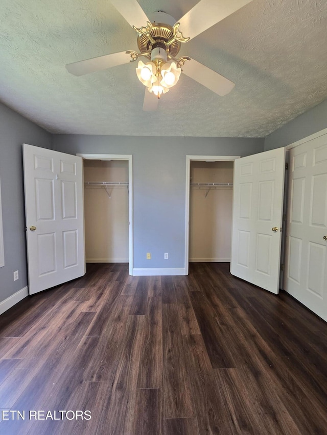 unfurnished bedroom featuring dark wood finished floors, a textured ceiling, multiple closets, and baseboards