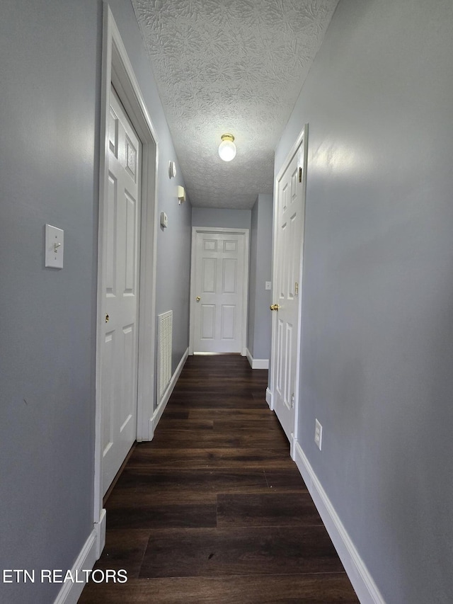 corridor featuring baseboards, wood finished floors, visible vents, and a textured ceiling