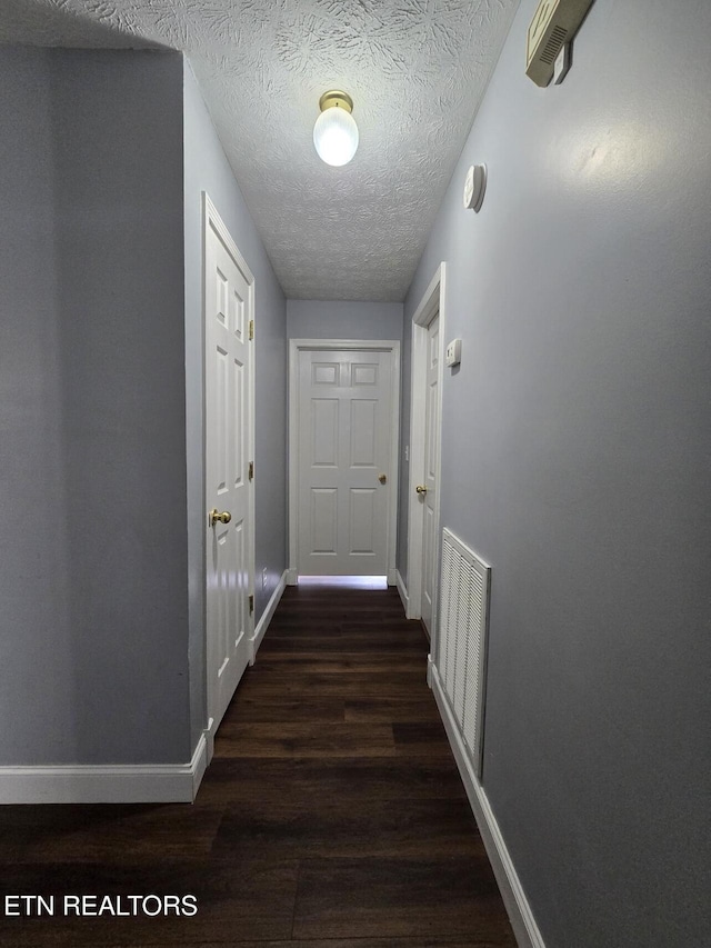 hall featuring baseboards, wood finished floors, visible vents, and a textured ceiling