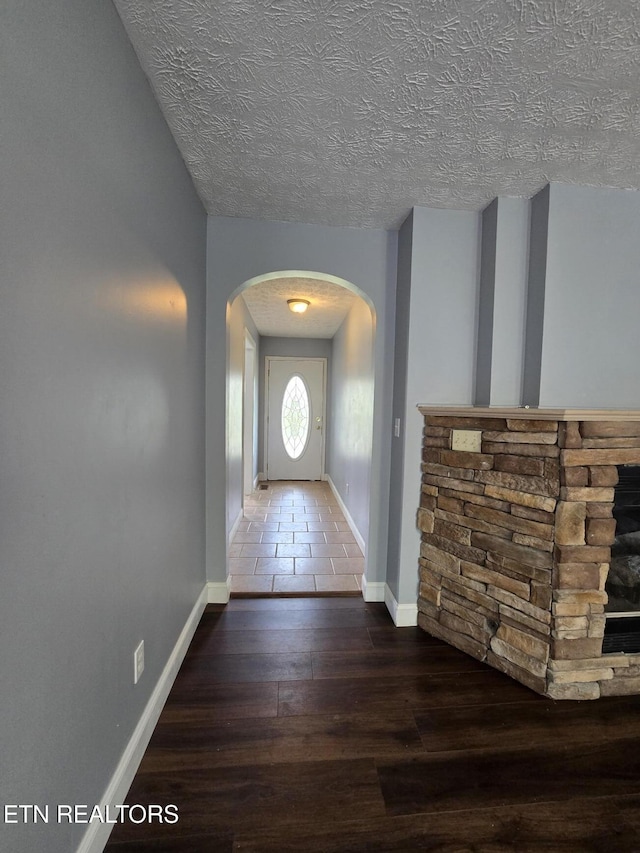 foyer featuring arched walkways, wood finished floors, a textured ceiling, and baseboards