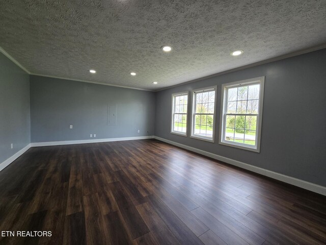 empty room with dark wood finished floors, a textured ceiling, crown molding, and baseboards