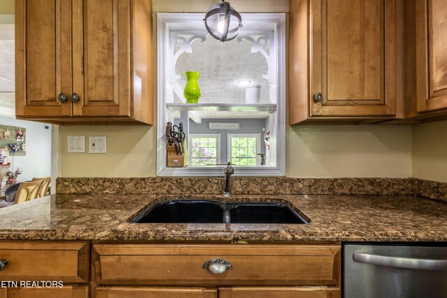 kitchen featuring stainless steel dishwasher, brown cabinetry, dark stone counters, and a sink