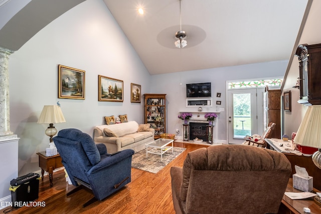 living area with a fireplace with flush hearth, high vaulted ceiling, ornate columns, and wood finished floors