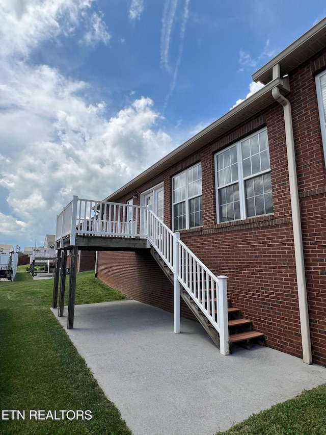 exterior space featuring brick siding, stairs, a yard, and a deck