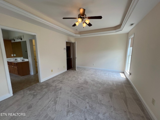 unfurnished bedroom featuring light carpet, baseboards, ensuite bathroom, a tray ceiling, and visible vents