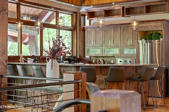 kitchen with backsplash, a breakfast bar, wood finished floors, freestanding refrigerator, and glass insert cabinets