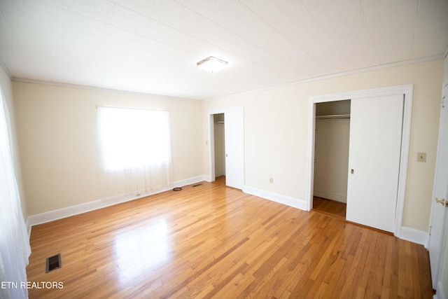 unfurnished bedroom featuring light wood-type flooring, visible vents, baseboards, and multiple closets