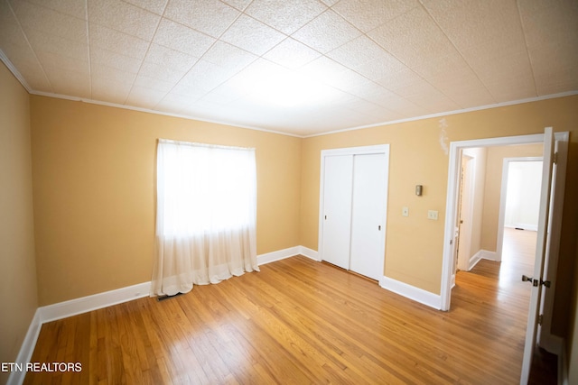 unfurnished bedroom with light wood-style flooring, baseboards, a closet, and ornamental molding