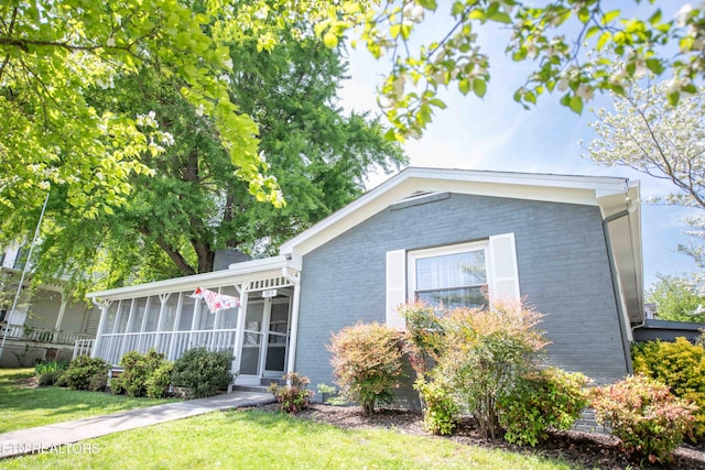 single story home featuring a front lawn, a sunroom, and brick siding