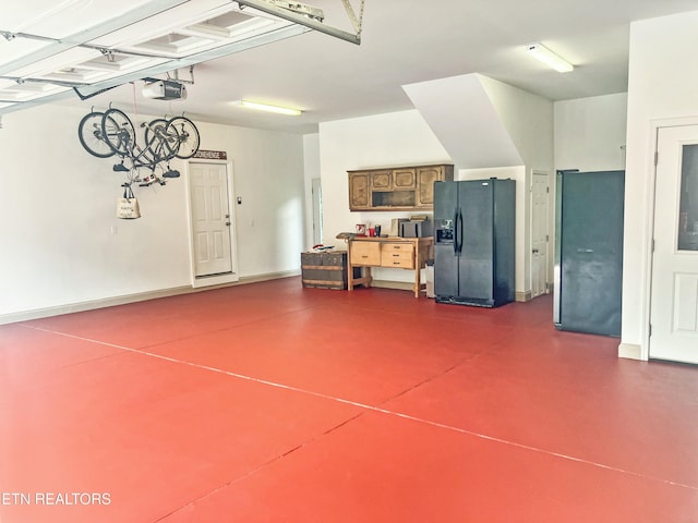 garage featuring black fridge with ice dispenser, a garage door opener, and baseboards