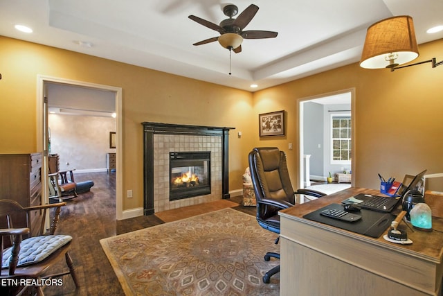 office featuring recessed lighting, a tile fireplace, a tray ceiling, wood finished floors, and ceiling fan