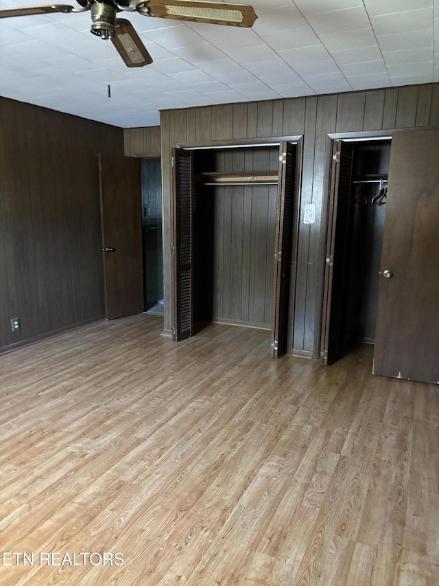 unfurnished bedroom with wood walls, wood finished floors, and multiple closets