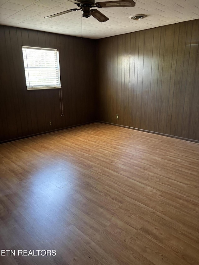 empty room featuring wood finished floors, visible vents, wooden walls, and ceiling fan