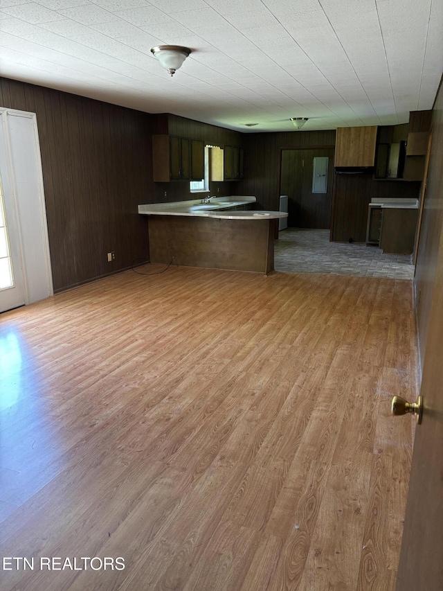 kitchen featuring light wood-type flooring, a peninsula, and wooden walls