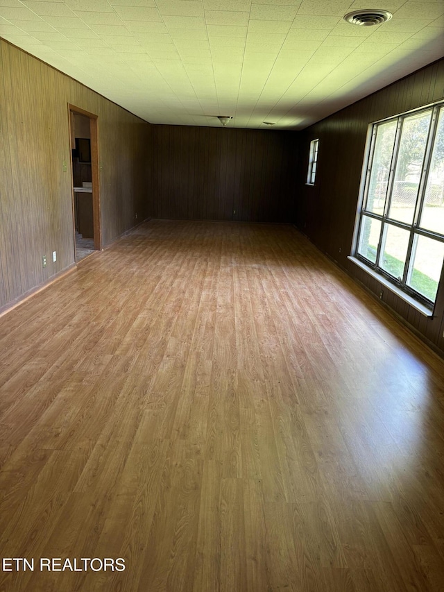 unfurnished room with wood walls, wood finished floors, and visible vents