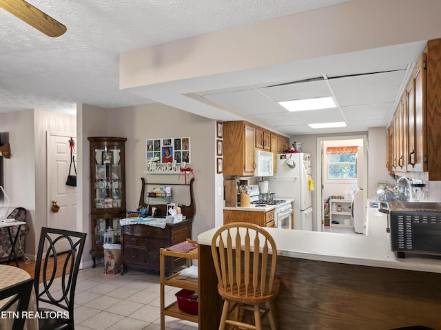 kitchen with brown cabinets, light countertops, baseboards, white appliances, and light tile patterned flooring