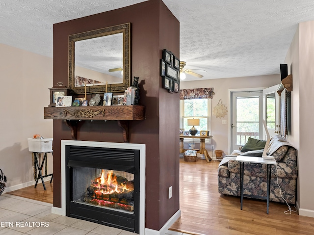 interior space featuring a warm lit fireplace, a textured ceiling, baseboards, and ceiling fan