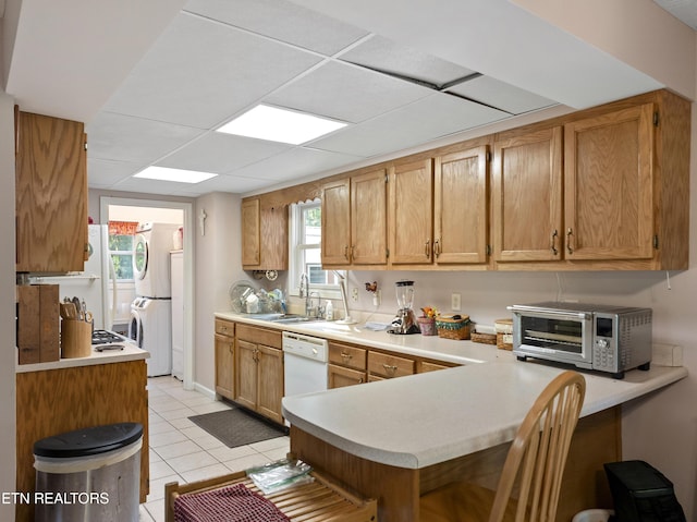 kitchen featuring stacked washer and dryer, dishwasher, a toaster, a sink, and a peninsula