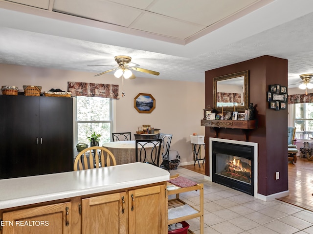 kitchen featuring a glass covered fireplace, a textured ceiling, a ceiling fan, and light tile patterned flooring