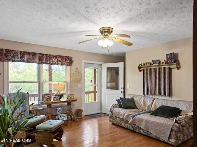 living room with a textured ceiling, ceiling fan, and wood finished floors