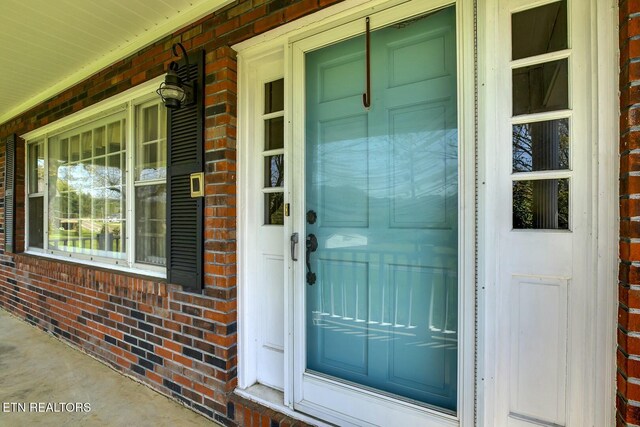 doorway to property featuring brick siding and covered porch