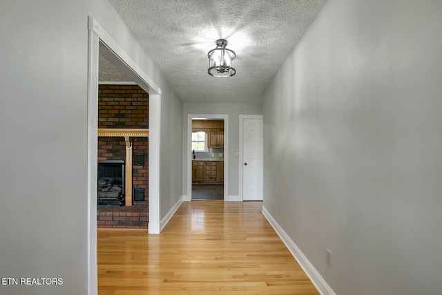 corridor with light wood-type flooring, a textured ceiling, and baseboards