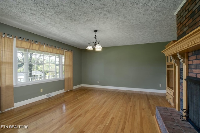 unfurnished living room with baseboards, a notable chandelier, light wood-style flooring, and a fireplace