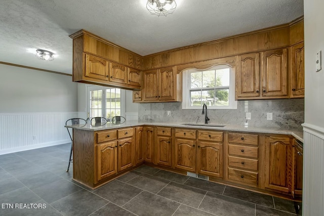 kitchen featuring a peninsula, a textured ceiling, a sink, and brown cabinets