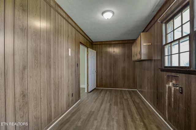 hallway featuring baseboards, dark wood-style flooring, and wooden walls