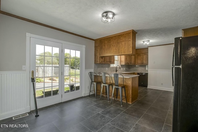 kitchen with a peninsula, a wainscoted wall, freestanding refrigerator, and crown molding
