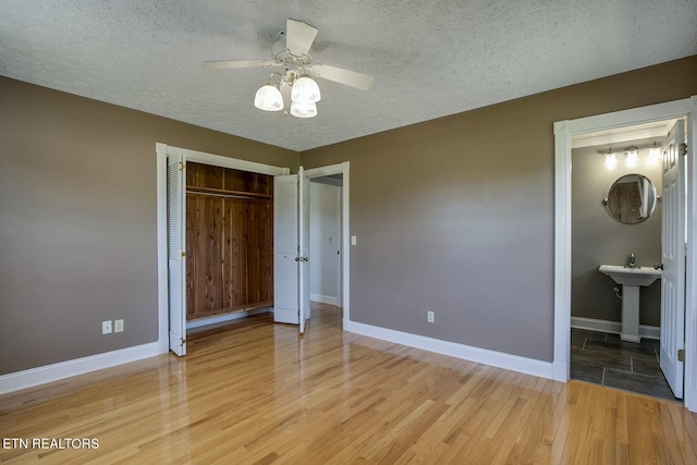 unfurnished bedroom with light wood finished floors, a textured ceiling, baseboards, a ceiling fan, and a closet