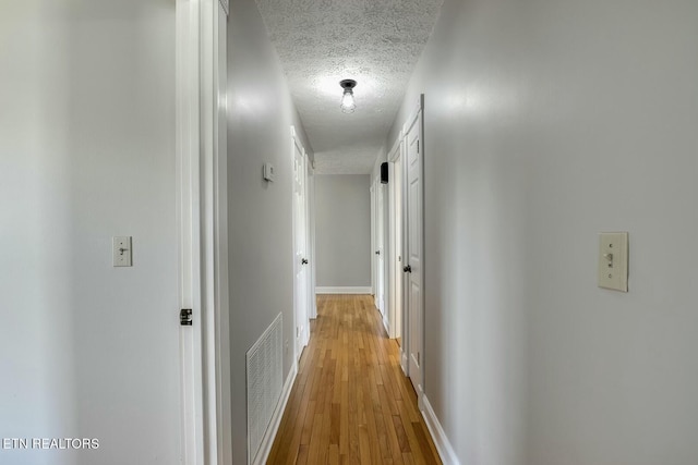 corridor featuring light wood finished floors, baseboards, visible vents, and a textured ceiling