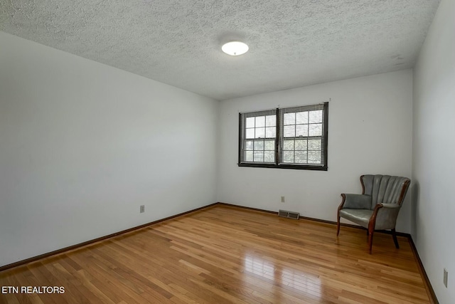 interior space featuring baseboards, light wood finished floors, a textured ceiling, and visible vents
