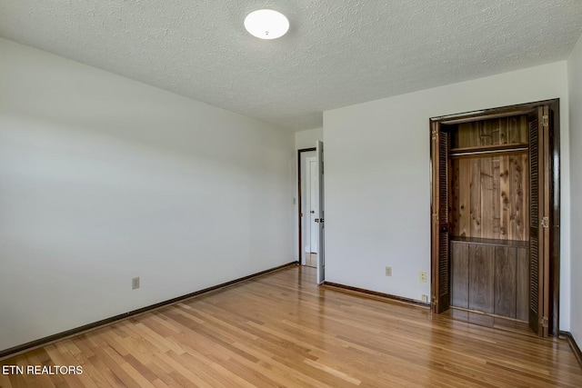 unfurnished bedroom with baseboards, light wood-style floors, a textured ceiling, and a closet