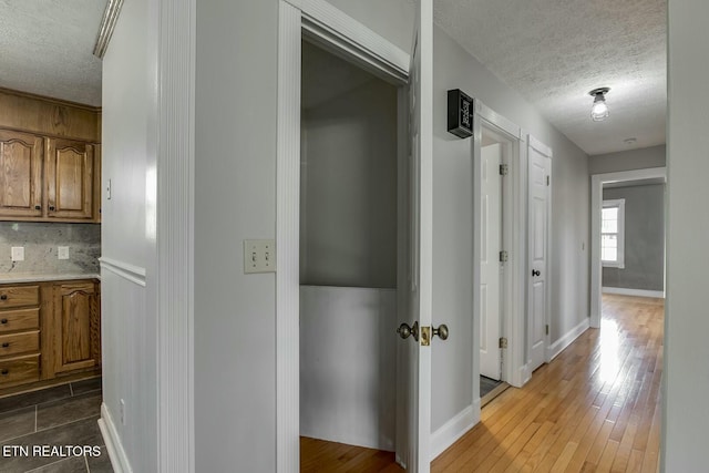 hall with wood finished floors, a textured ceiling, and baseboards