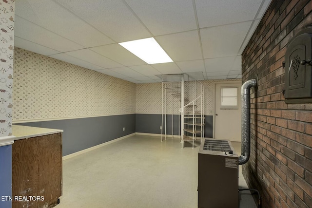 below grade area with wallpapered walls, a drop ceiling, and baseboards